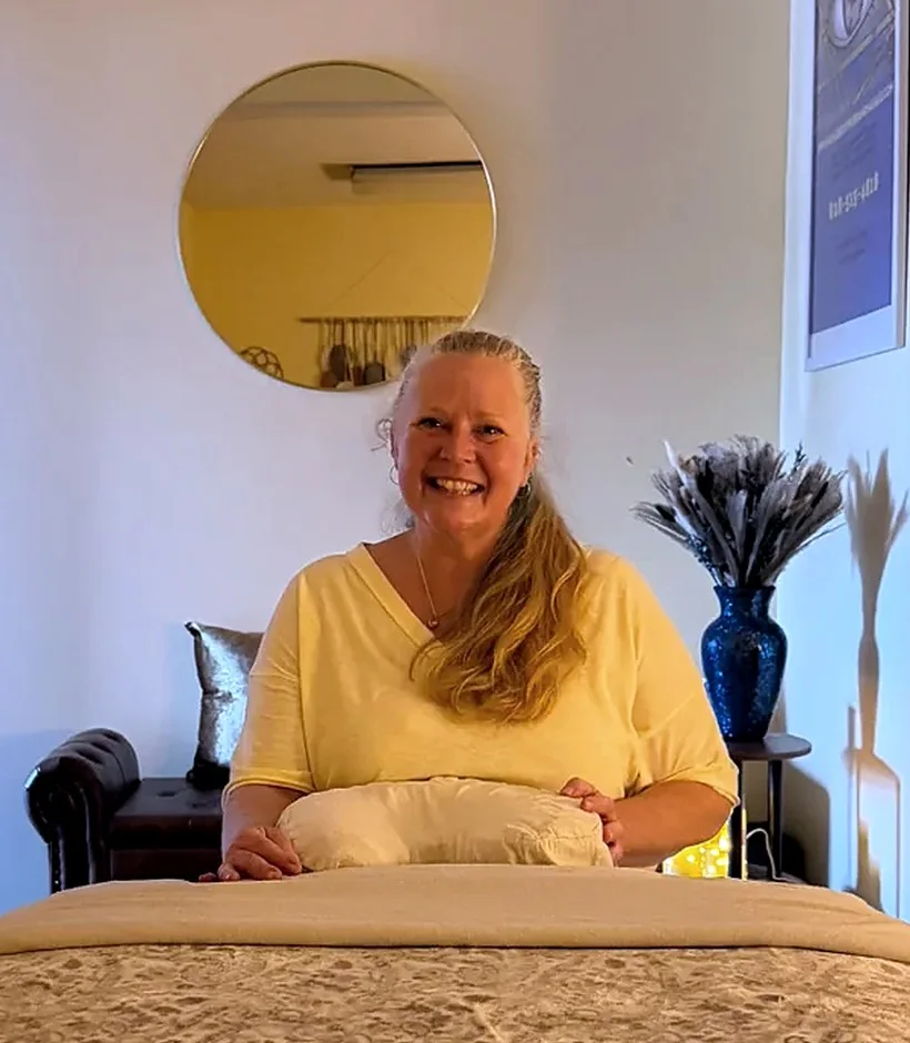Molly smiling behind the massage table in her treatment room